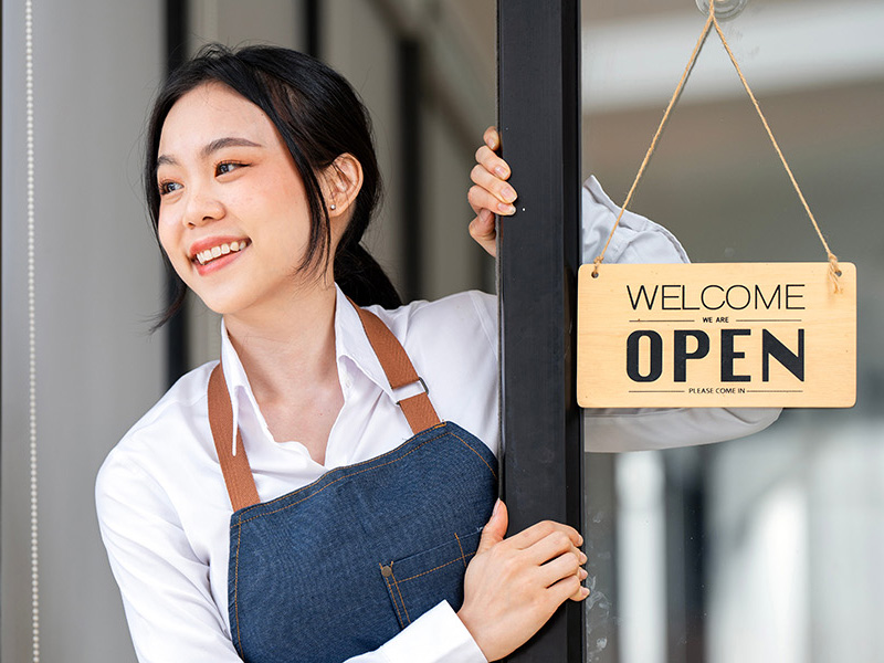 Young Asian woman at door with Open sign